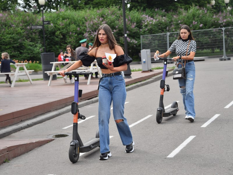 На фото две девушки ведут самокаты в велодорожке