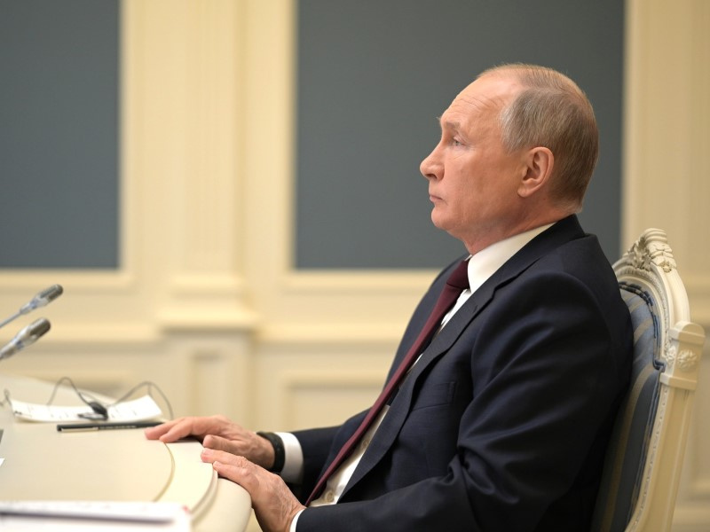 На фото Володя Путин сидит в анфас на стуле и держит ладони на краю стола