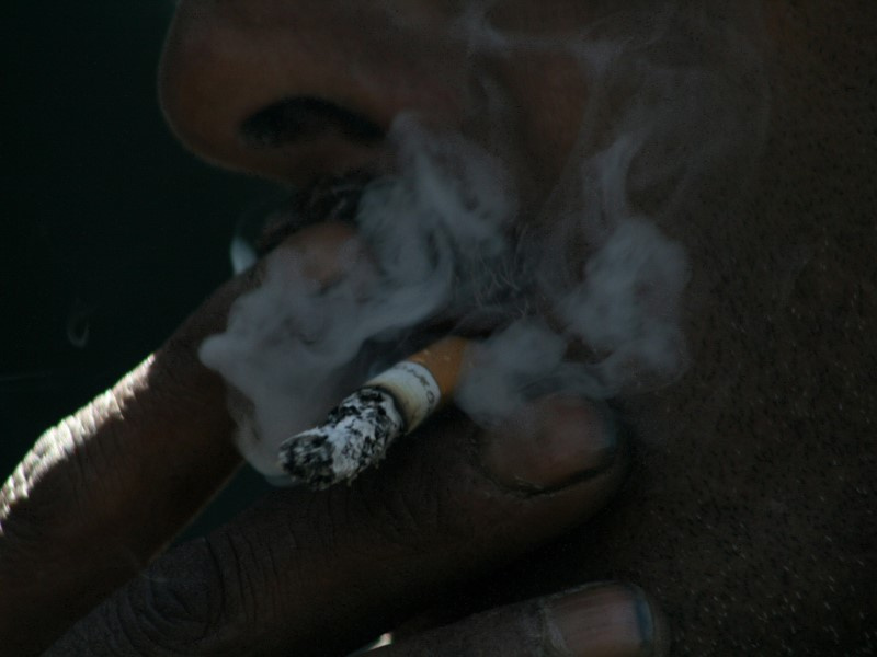 На фото крупный план курящего мужчины с грязью под ногтями