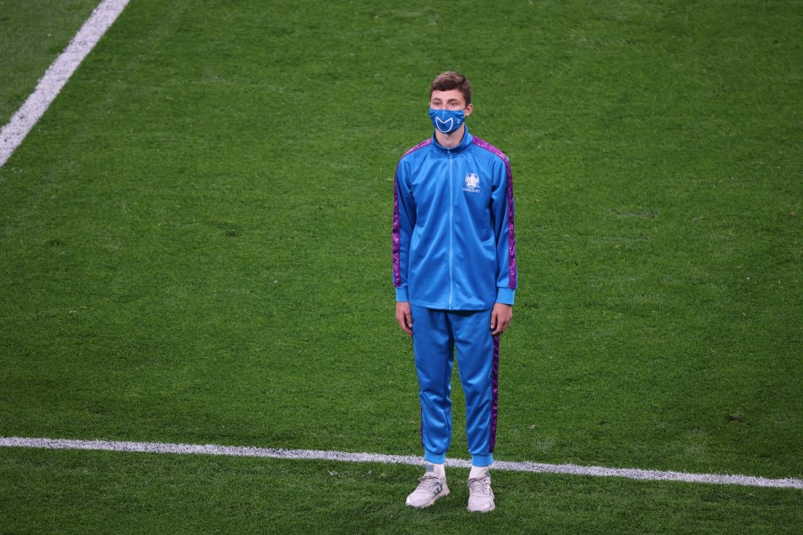 На фото молодой человек в синем спортивном костюме и в синей маске стоит на поле